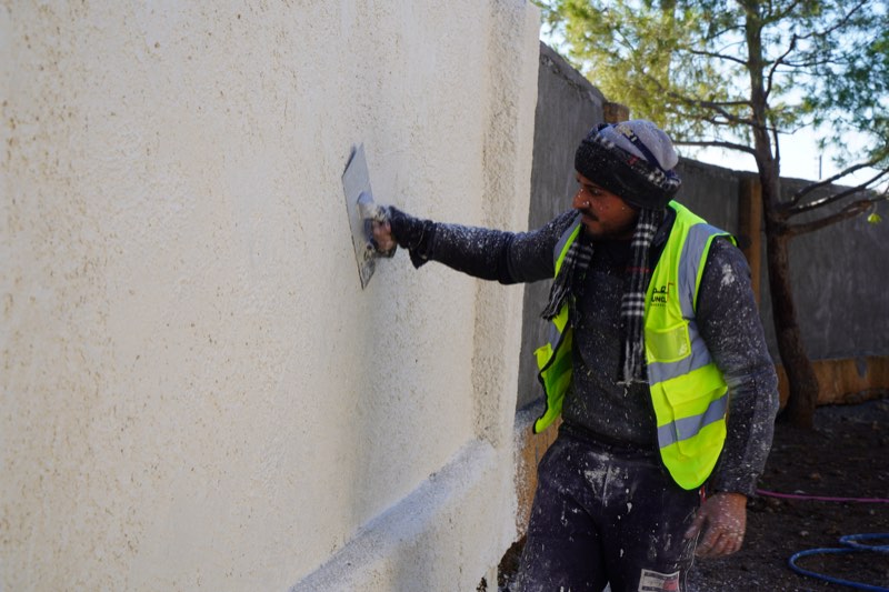 A worker plastering a school wall